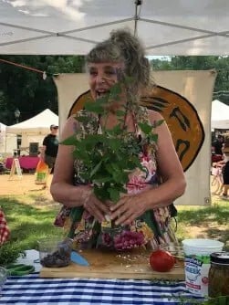 Susan Belsinger at an outside table holding anise hyssop plant