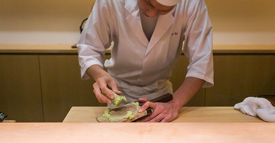 Person preparing wasabi paste in a professional kitchen setting.