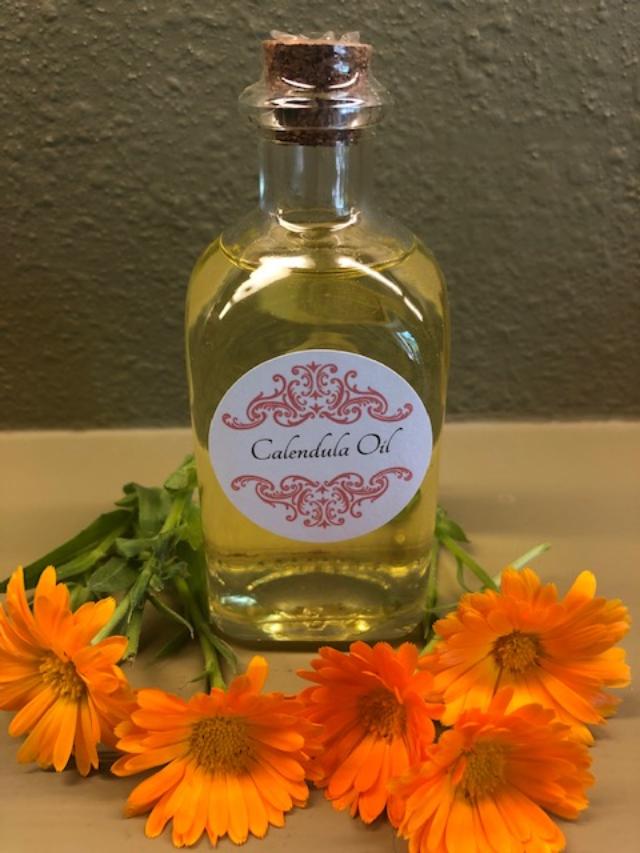 Glass bottle of light yellow oil surrounded by orange flowers