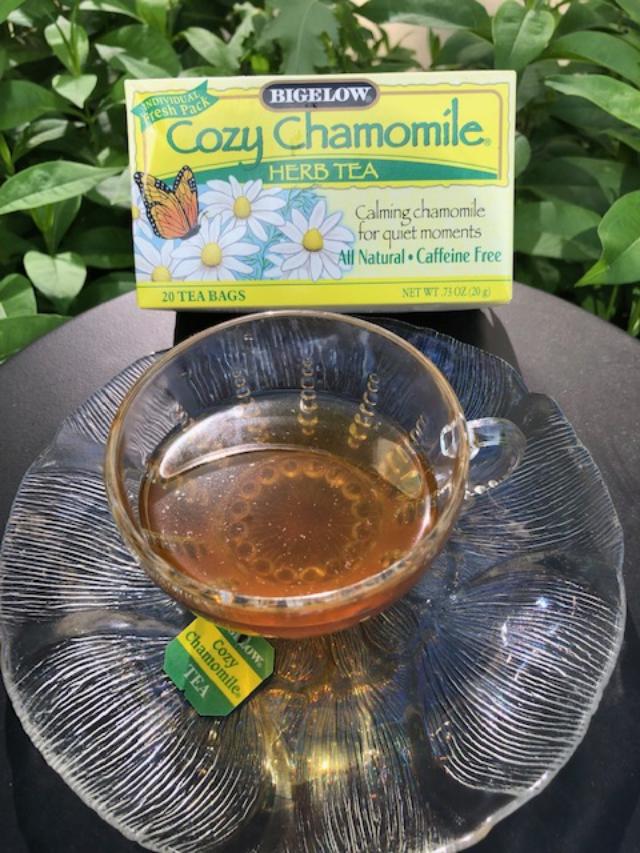 A glass teacup and saucer full of chamomile tea, with a box of chamomile tea nearby