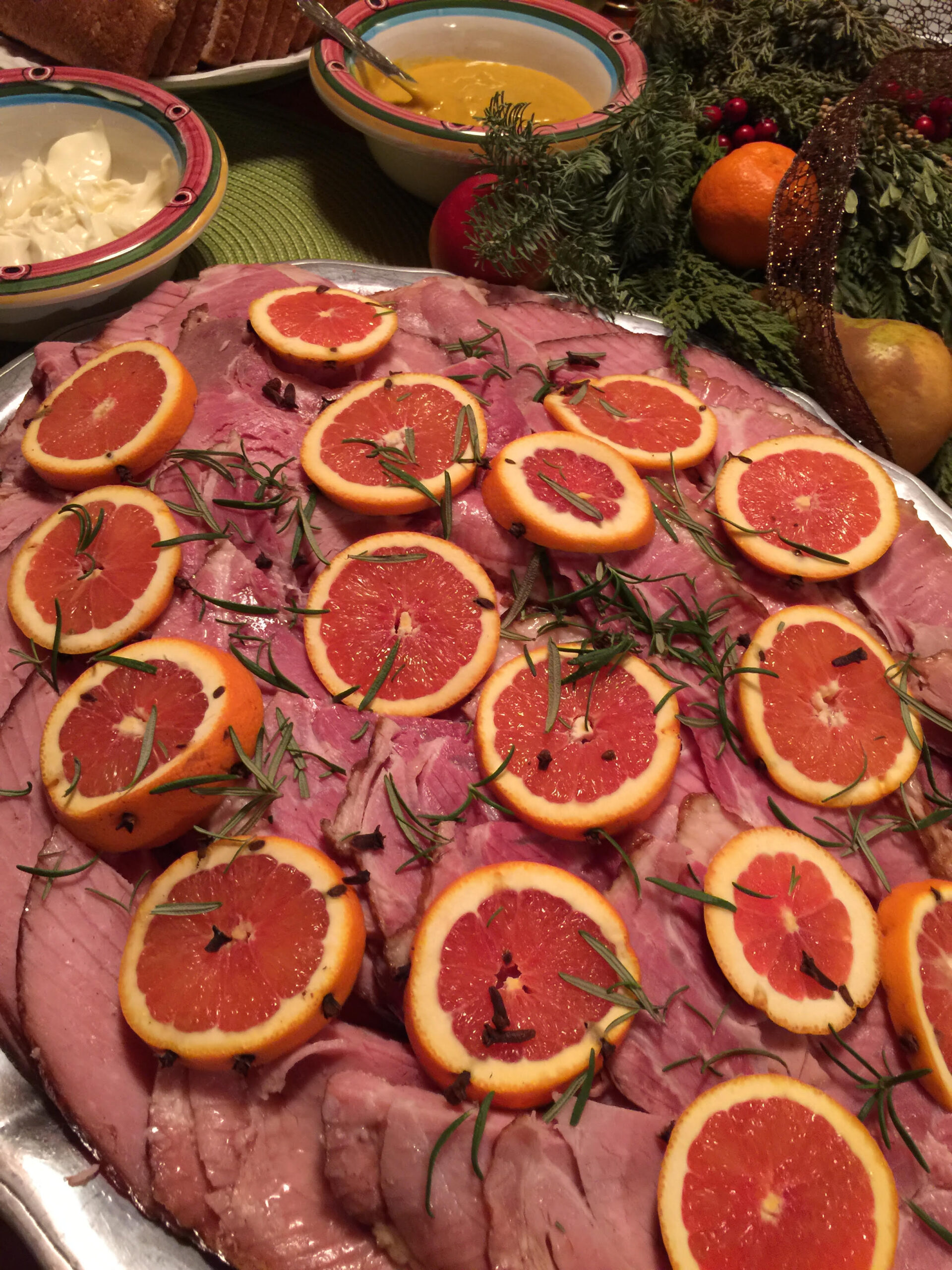 A platter of ham with citrus rounds and rosemary