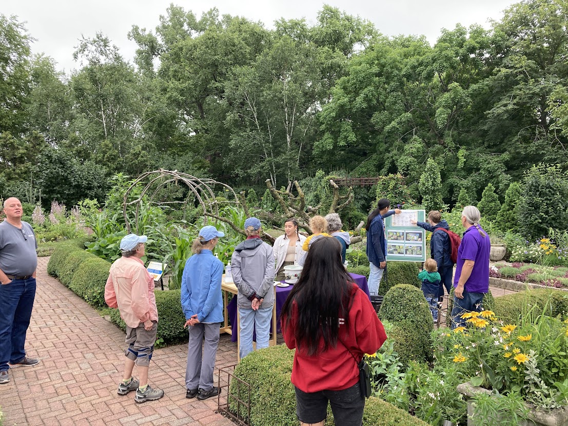 A group of people in a garden listening to a presentation.
