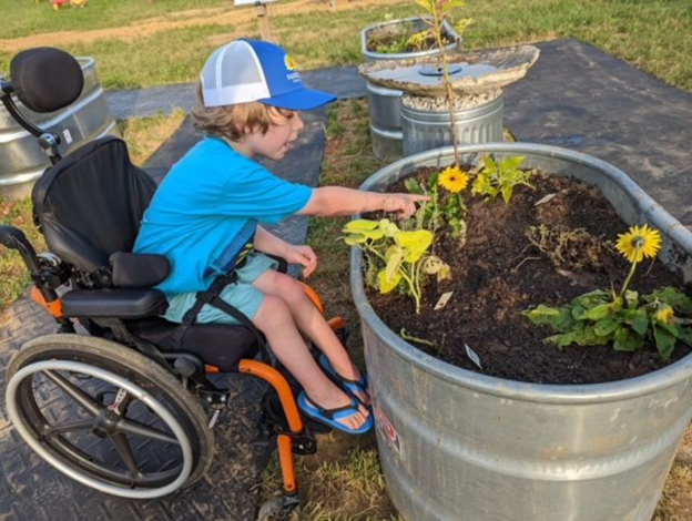 A child in a wheelchair points to a yellow flower in a raised bed