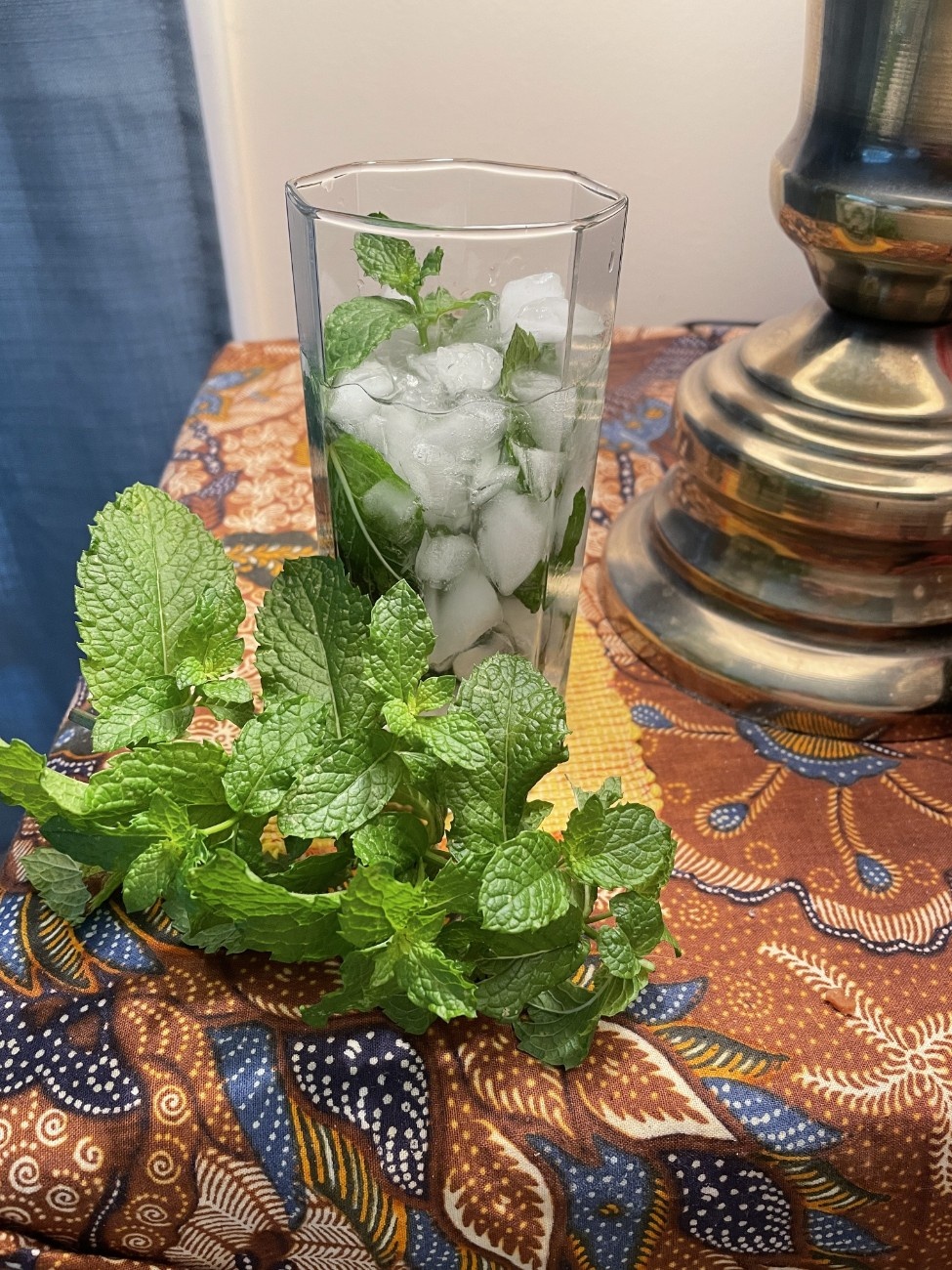 A clear glass full of ice cubes and mint leaves sits on a table