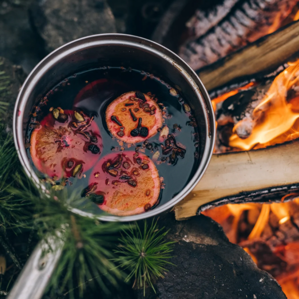 A small pot with wine and mulling spices sits next to a fire
