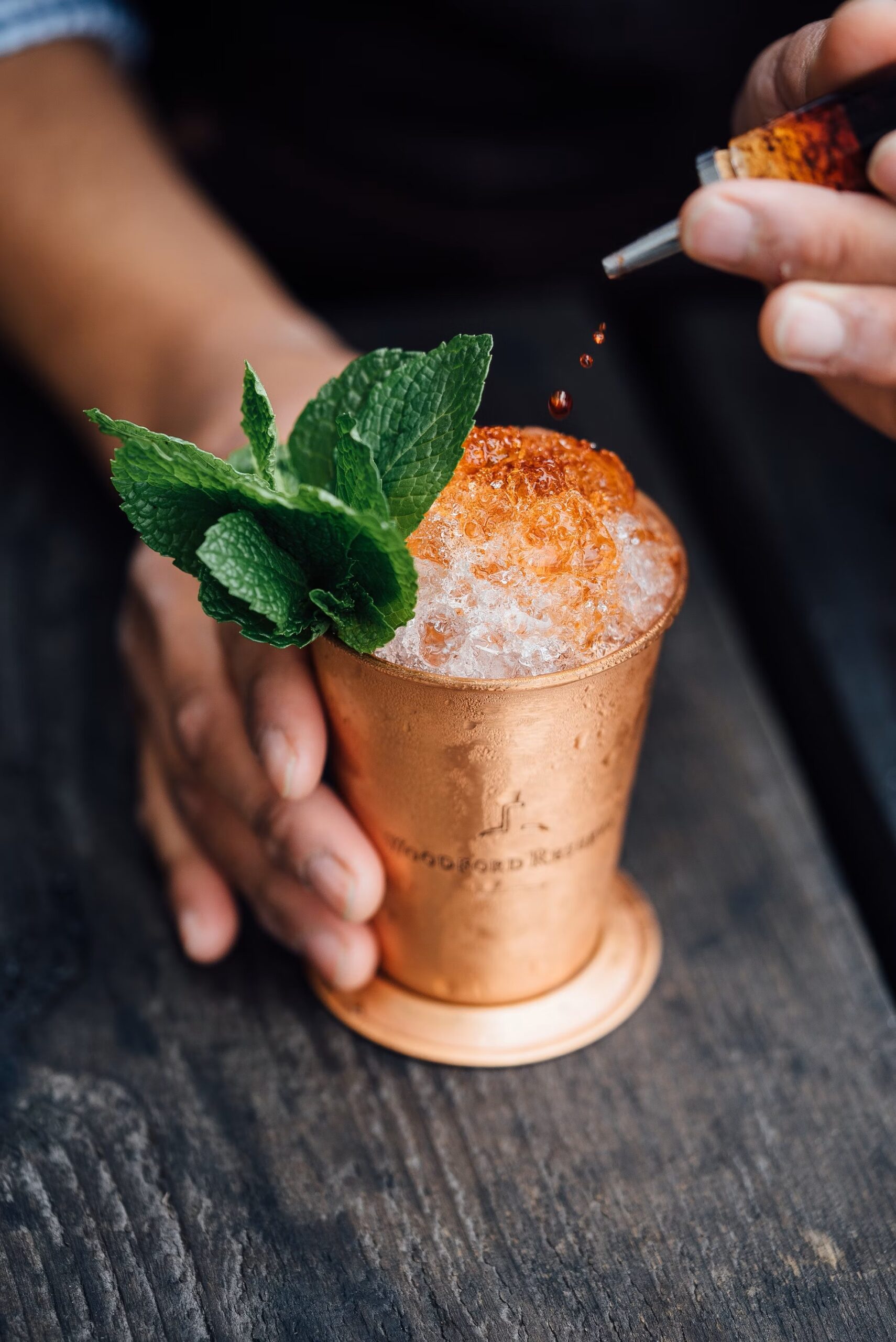 Bitters being dashed onto a cocktail in a copper cup with a mint sprig