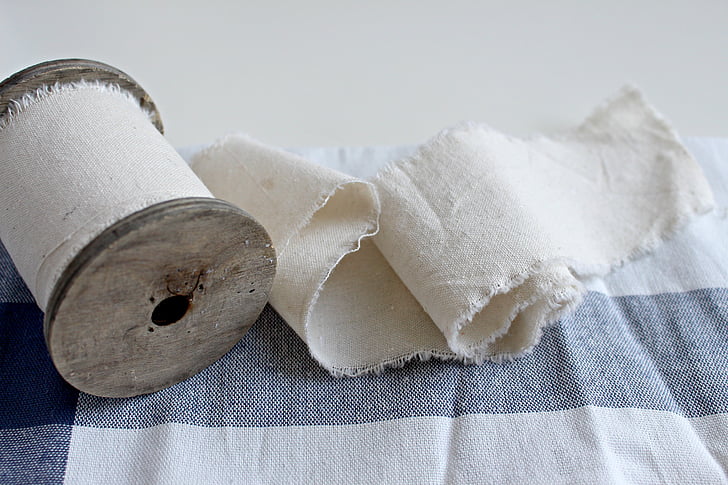 A spool of white cotton fabric on a blue and white tablecloth