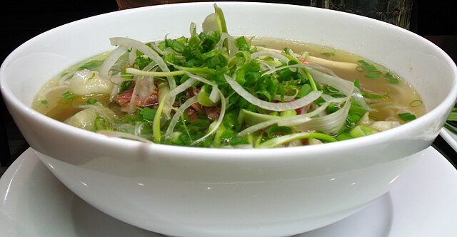 A white ceramic bowl of pho, with slivers of onion on top.
