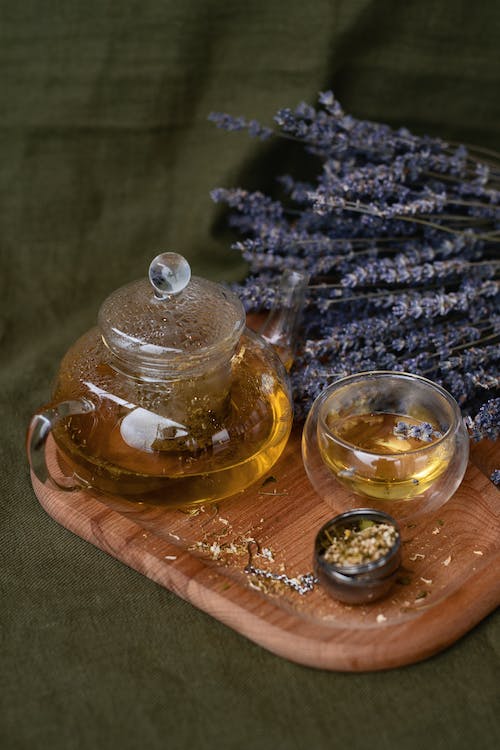 A glass teapot on a wooden tray with a bouquet of lavender