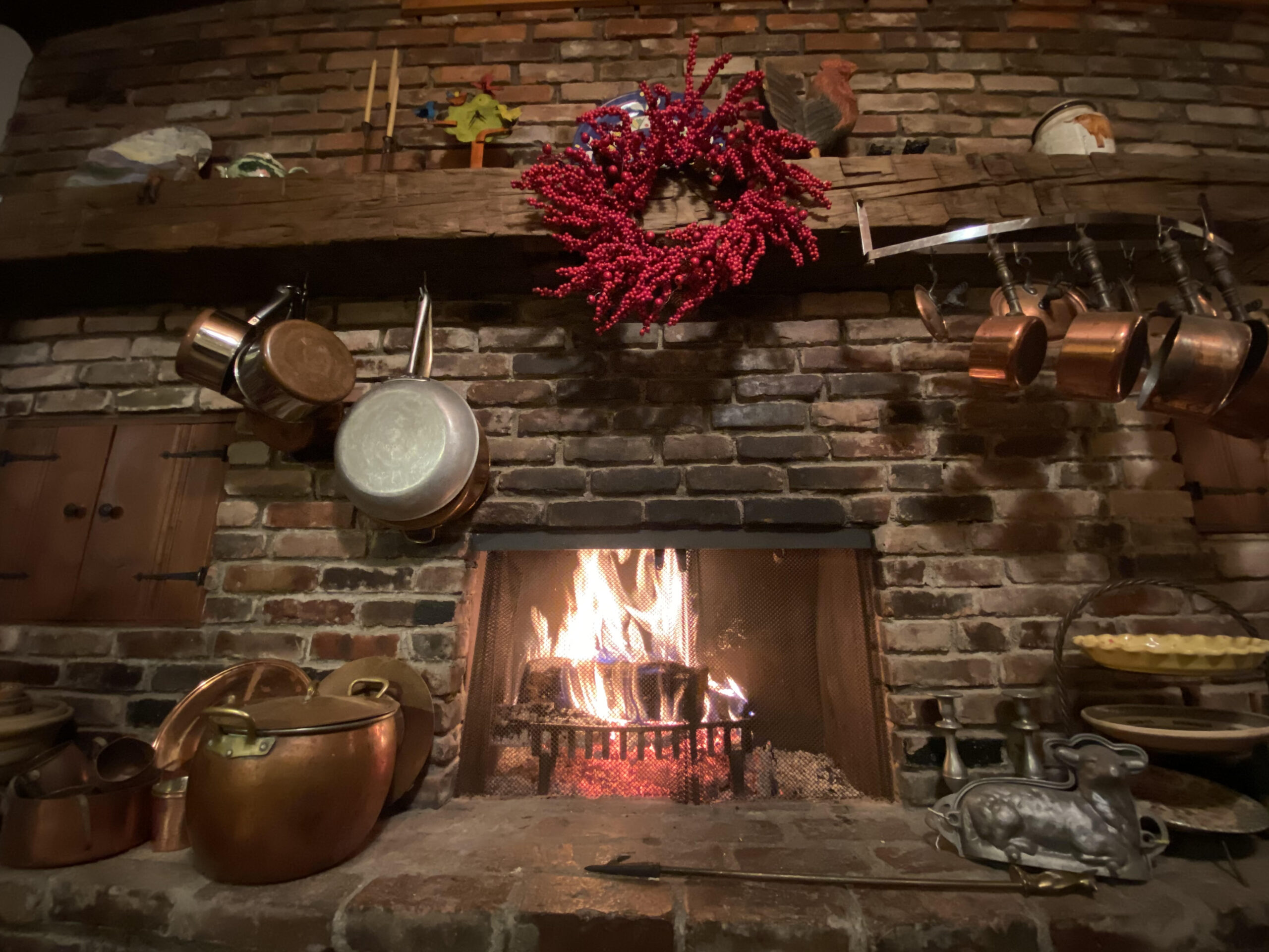 A brick fireplace with a red berry wreath above it on the mantle