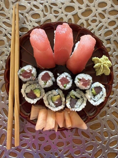 Assorted sushi rolls with wasabi and pickled ginger on a decorative plate.
